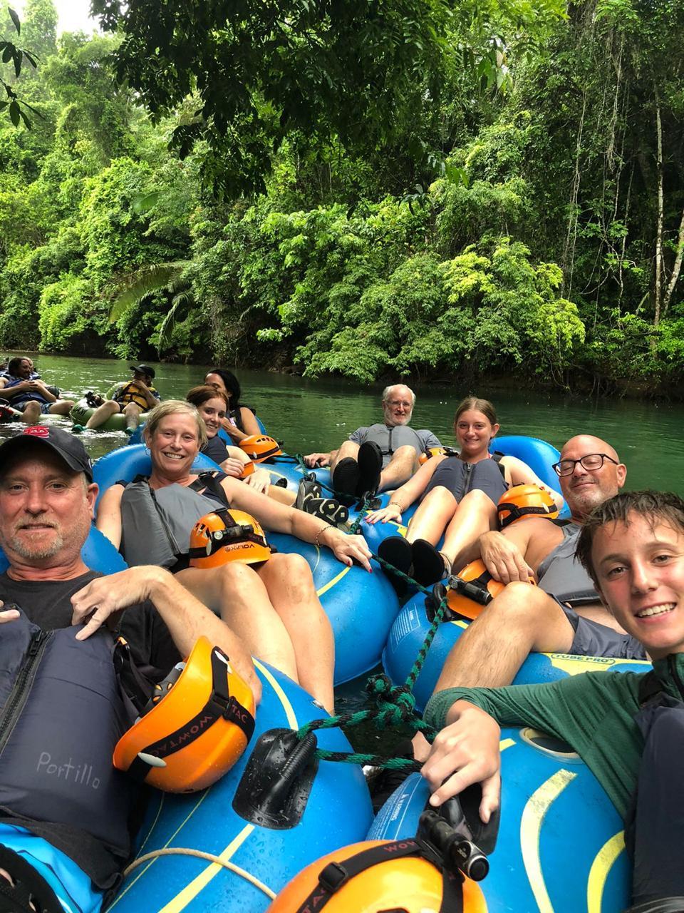 Family and friends in helmets and life jackets smiling together as they float on blue tubes down a jungle river