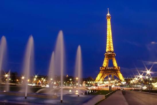 The Eiffel Tower lit gold at night above glowing fountains in Paris