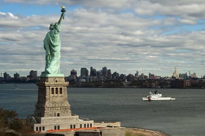 The Statue of Liberty on its pedestal, with a coast guard vessel and the New York skyline across the harbor