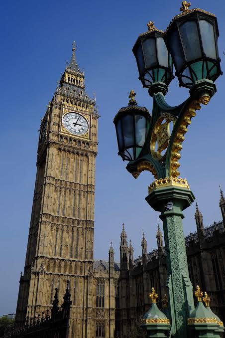 The Big Ben clock tower rising beside an ornate green and gold lamppost against a deep blue sky in London