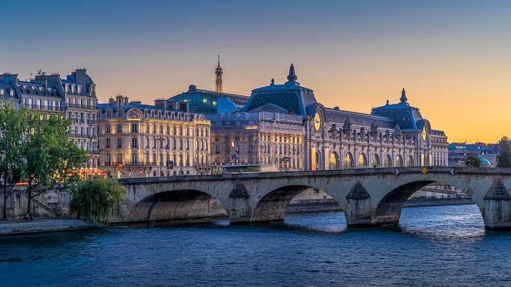 Dusk over the Seine in Paris, with a stone bridge, a grand riverside building and the Eiffel Tower faint in the distance